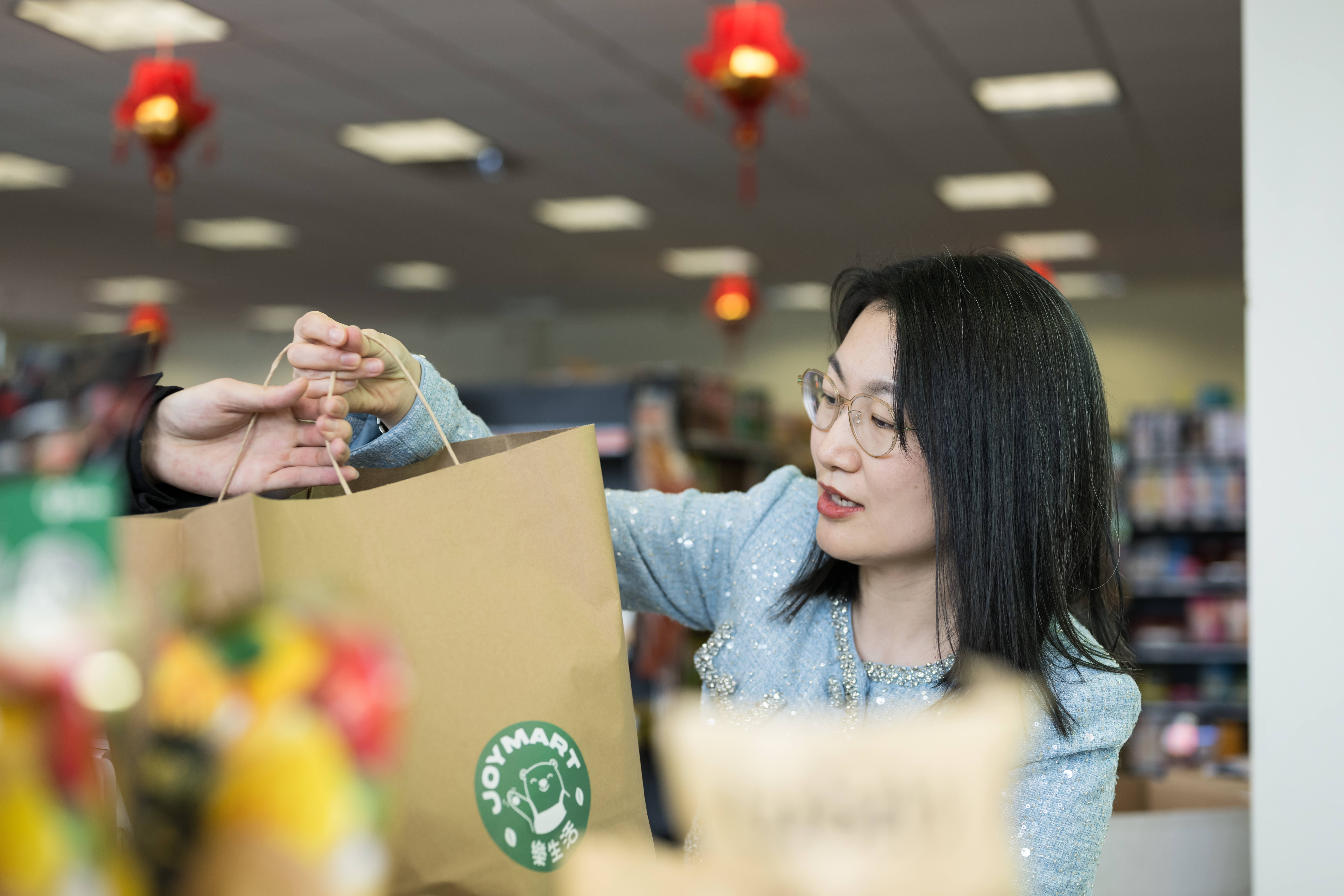 Vicki Liang hands customer a bag of groceries at the register.