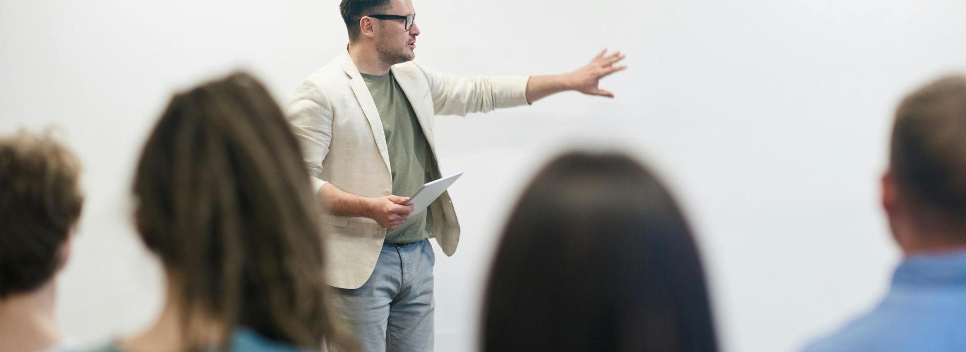 A man is presenting something, that is out of the frame of the photo, to a seated audience.