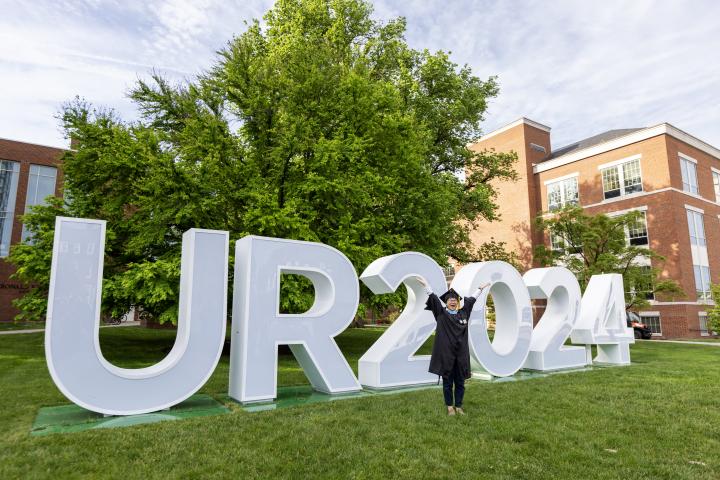 Graduate standing in front of UR2024 signage and LeChase Hall