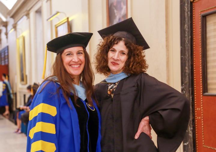Two women, one a master's student and the other a doctoral student, posing together, smiling and dressed in graduation gowns.